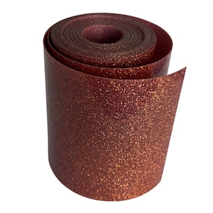May include: A roll of shimmering, glittery, copper-colored ribbon. The ribbon is tightly rolled, revealing the inner layers and the textured surface of the material. The glitter catches the light, creating a sparkling effect.