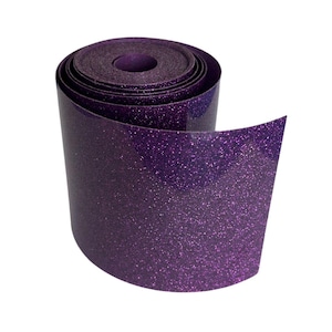 May include: A roll of purple glitter vinyl. The vinyl is rolled up, with the end unrolled, showing the shiny, textured surface. The glitter is evenly distributed across the surface, creating a sparkling effect. The roll is set against a white background.