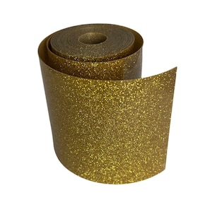 May include: A roll of gold glitter paper, unrolled to reveal the shiny surface. The paper is a warm gold color and has a textured, sparkling appearance. The roll is partially unraveled, showing the inner core.