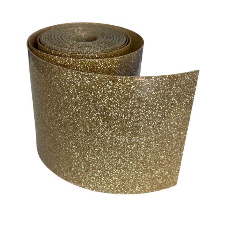 May include: A roll of gold glitter ribbon. The ribbon is tightly wound, with the end unfurled, revealing the glittery texture. The gold color is consistent throughout, creating a shimmering effect. The background is white.