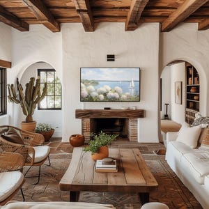 May include: A cozy living room with a fireplace, a large wooden coffee table, and two wicker chairs. A TV displays a scenic view. The room features a neutral color palette with wooden beams and a cactus plant.