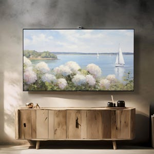 May include: A large, flat-screen television displays a serene landscape painting of a sailboat on the water, with white flowers in the foreground. The TV is mounted above a light-colored wooden cabinet with a natural finish. Decorative items sit on top of the cabinet.