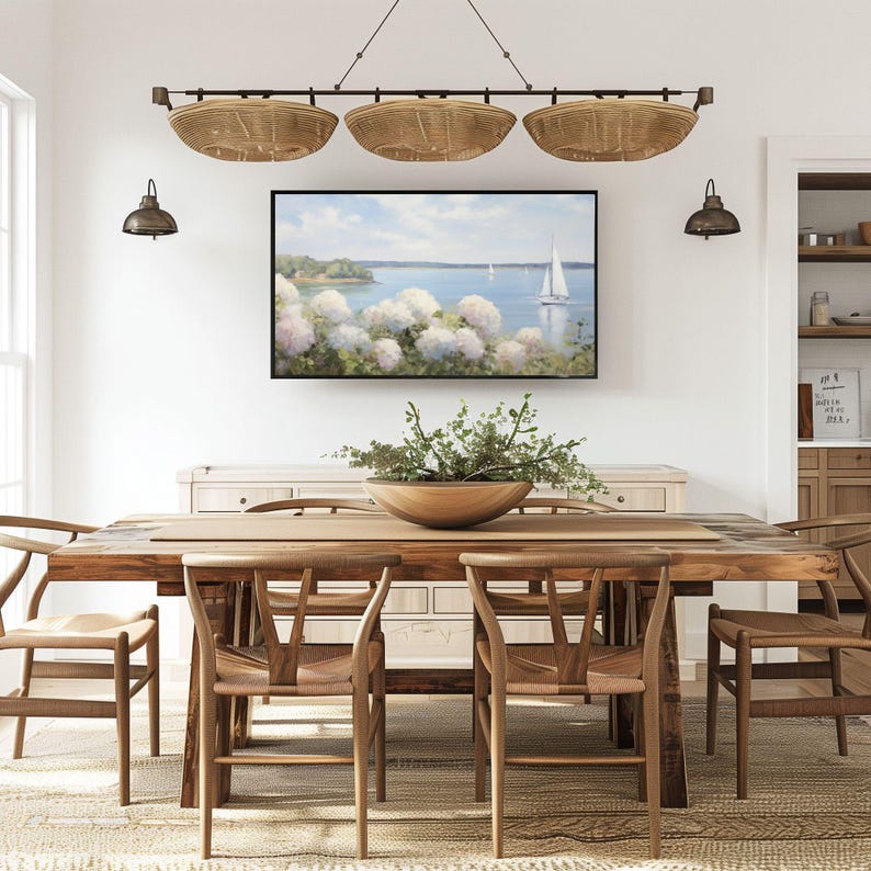 May include: A dining room scene featuring a large wooden table with woven chairs. Above the table hangs a light fixture with three woven basket shades. A framed landscape painting of a sailboat on the water is centered on the wall.