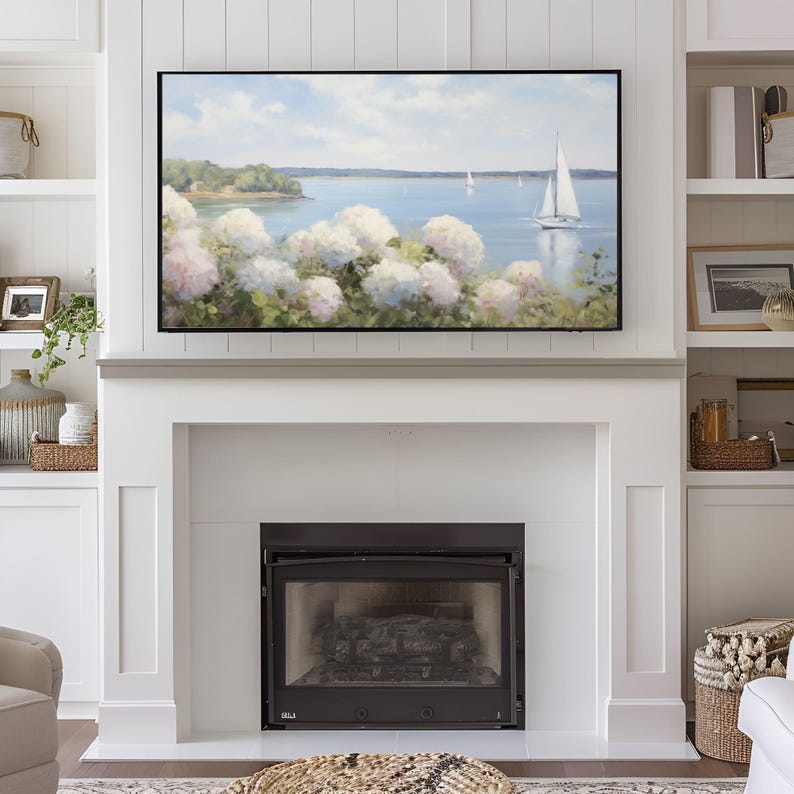 May include: A framed landscape painting of a serene coastal scene with sailboats on the water. White hydrangeas bloom in the foreground, with a backdrop of a blue sky and green trees. The painting is displayed above a white fireplace.