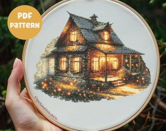 May include: A cross-stitch pattern of a cozy cabin with glowing windows and a warm, inviting atmosphere. The design is set in a wooden embroidery hoop. The text "PDF PATTERN" is in a yellow circle. The text "CopelandStitchCo." is on the hoop.
