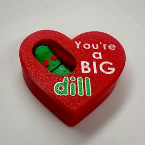 May include: Red heart-shaped box with a green pickle inside. The box says "You're a BIG dill" in white letters.