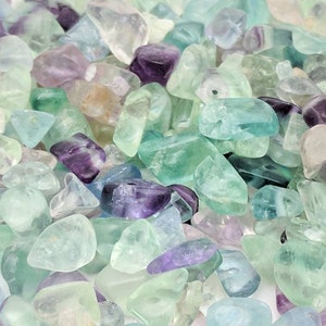 May include: A close-up view of a pile of fluorite chips in various shades of green, blue, and purple. The chips are tumbled and have a smooth, polished finish.