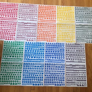 May include: A set of ten sheets of alphabet stickers in various colors, including red, orange, yellow, green, blue, and black. Each sheet features uppercase letters, numbers, and punctuation marks.