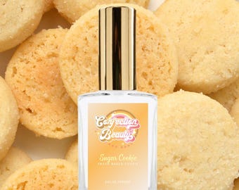 May include: A glass bottle of Sugar Cookie scented perfume with a yellow and orange label that says "Confection Beauty" and "Sugar Cookie Fresh Baked Cookie Eau de Parfum". The bottle is surrounded by sugar cookies.
