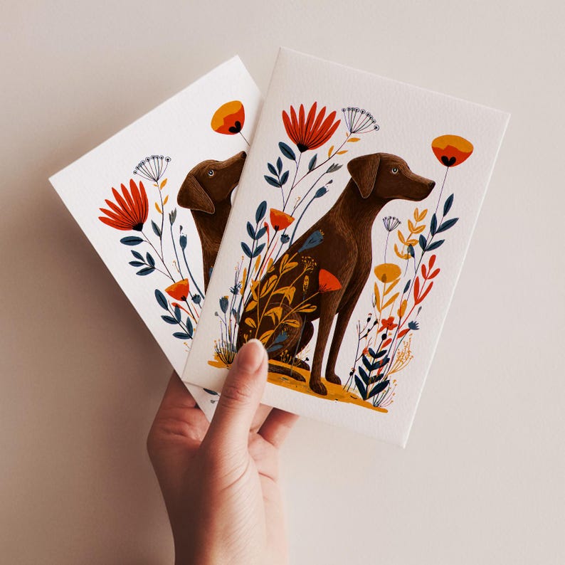 May include: Two white rectangular greeting cards featuring a brown dog illustration surrounded by stylized red, orange, and dark blue flowers and foliage. The dog is depicted in a seated position, facing right, amidst a colorful botanical arrangement.