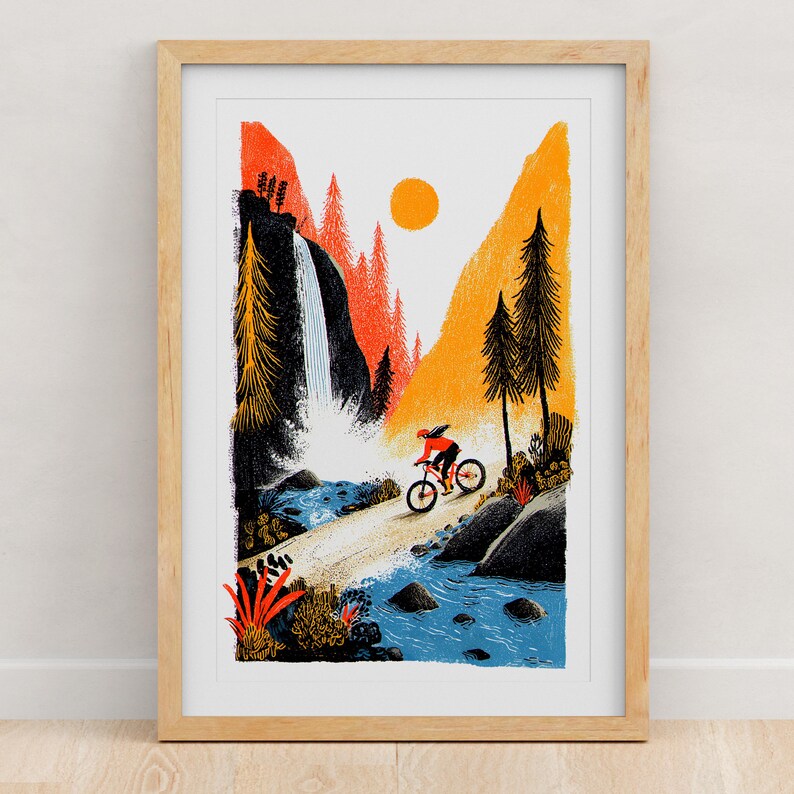 Pu&ograve; includere: Una stampa artistica incorniciata che presenta un'illustrazione stilizzata di un ciclista su una mountain bike lungo un sentiero vicino a una cascata. La scena include montagne arancioni e gialle, alberi sempreverdi scuri e un fiume blu.