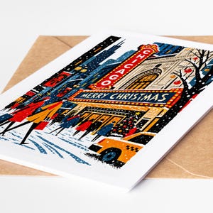 Chicago Christmas card lying on a kraft envelope, folk art Chicago Theatre marquee glowing over State Street in the snow