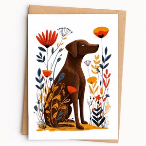 May include: A greeting card featuring a brown dog sitting in a field of stylized flowers. The illustration includes tall red, orange, and blue floral stems surrounding the dog, set against a plain white background with a brown envelope behind it.