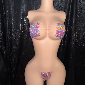 May include: A two-piece bikini set on a mannequin. The top and bottom are covered in colorful sequins. The top is a bandeau style with clear straps, and the bottom is a thong style with clear straps.