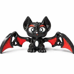 May include: A black bat figurine with red wing accents. The bat has large, expressive eyes, red eyebrows, and a white spot on its chest. The wings are spread, and the figurine is set against a white background.