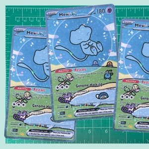 May include: Three Pokemon trading cards featuring a light blue Mew character. The cards have a blue and white background with the text "Mew EX" and "Restart" visible. The cards are on a green cutting mat.