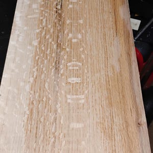 May include: A rectangular, unfinished wooden plank with a light brown color and visible wood grain. The wood has a natural, raw appearance, with a dark crack running down the center. The plank is likely for woodworking or DIY projects.
