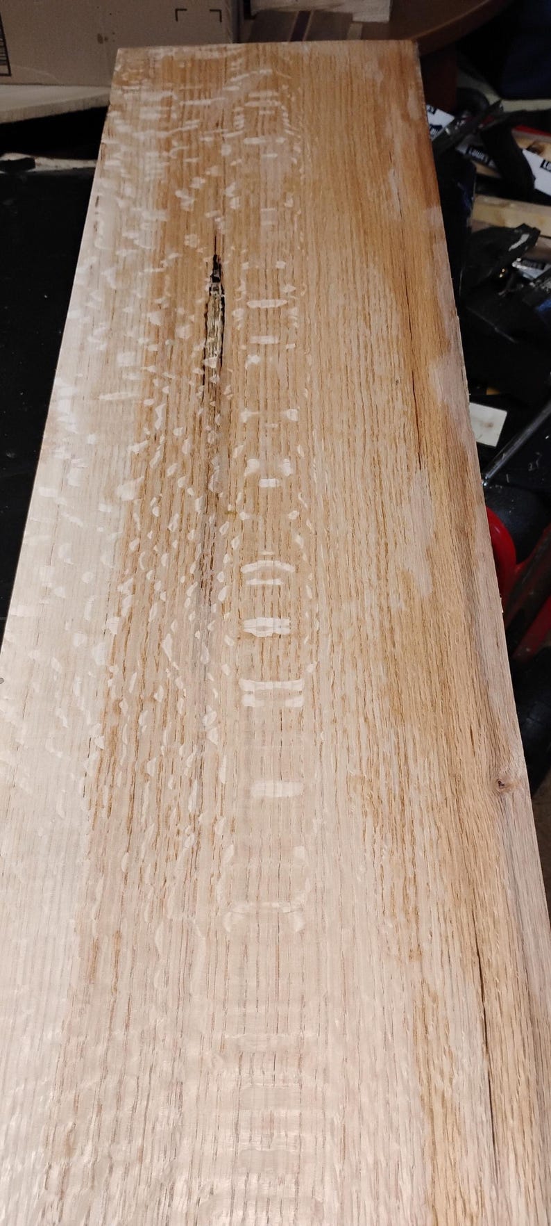 May include: A rectangular, unfinished wooden plank with a light brown color and visible wood grain. The wood has a natural, raw appearance, with a dark crack running down the center. The plank is likely for woodworking or DIY projects.