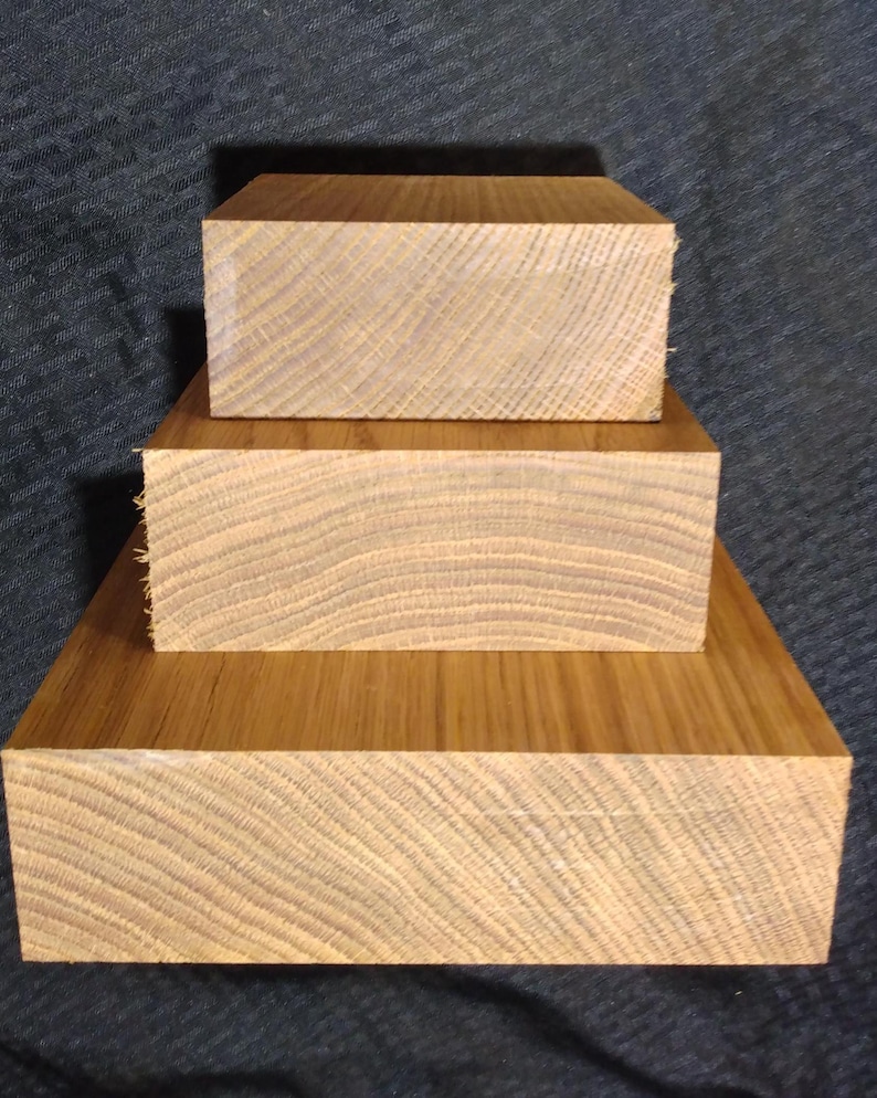 May include: Three stacked, rectangular wooden blocks with visible grain patterns. The blocks are a warm, light brown color, with the largest block at the base and the smallest on top. The wood appears to be unfinished.