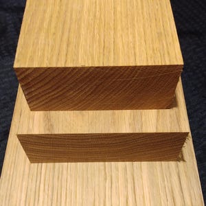 May include: Three pieces of unfinished oak wood. The largest piece is rectangular, with a smaller rectangular piece on top. A third, smaller piece is placed on top of the second piece. The wood grain is visible.