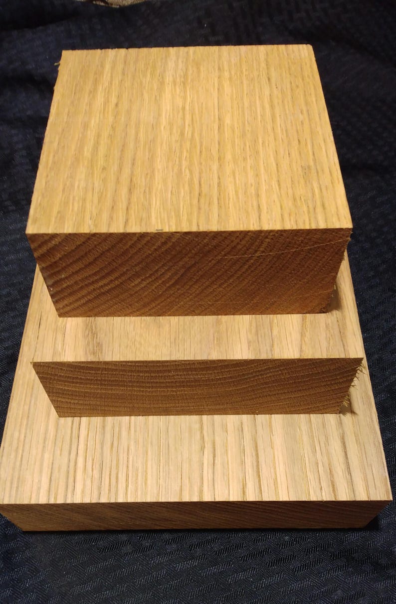 May include: Three pieces of unfinished oak wood. The largest piece is rectangular, with a smaller rectangular piece on top. A third, smaller piece is placed on top of the second piece. The wood grain is visible.