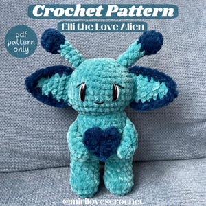 Puede incluir: Patrón de crochet para un extraterrestre amigurumi azul y turquesa que sostiene un corazón azul. El patrón se llama "Elli the Love Alien".