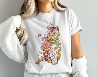 Puede incluir: Camiseta blanca con una ilustración de acuarela de un gato adornado con flores y mariposas. El pelaje del gato tiene diseños florales y de hojas. El diseño incluye varios colores, como rosa, naranja, verde y amarillo.