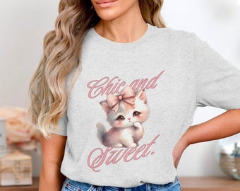 May include: Light gray t-shirt featuring a watercolor illustration of a kitten with a pink bow and the text "Chic and Sweet" in pink script. The kitten is white and pink.