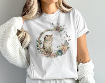 May include: White t-shirt with a watercolor illustration of a cat sitting in a wreath of flowers. The cat is brown and white with green eyes. The flowers are in shades of pink, blue, and green.