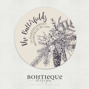 May include: A round, cream-colored sticker with a black and white illustration of pine branches, berries, and pine cones. The text "The Butterfields" is written in a cursive font above the illustration. The address "350 Fairfield Road, Brookfield, WI 53186" is written in a smaller font below the illustration. The text "BOHTIEQUE design" is written in a cursive font below the address. The website "www.bohtiequedesign.com" is written in a smaller font below the text "BOHTIEQUE design".