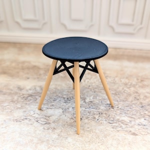 May include: A black round table with a geometric wooden base. The table has four legs and a black top.