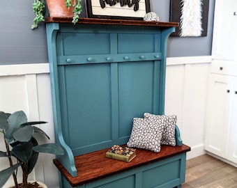 May include: A teal blue wooden hall tree with a bench seat, storage compartment, and coat hooks. The bench has two pillows with a black and white geometric pattern. The hall tree has a wooden top with a sign that reads "family".