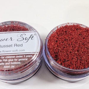 May include: Two clear plastic jars filled with russet red craft material. One jar is closed with a label that reads "Flower Soft Russet Red". The other jar is open, displaying the textured, red contents. The label also includes the website address and other text.
