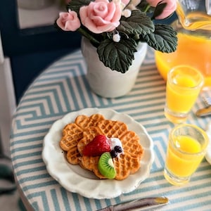 May include: A plate of heart-shaped waffles topped with whipped cream, strawberries, kiwi, and blueberries. The waffles are on a white plate with a blue and white checkered tablecloth. There is a glass of orange juice and a bouquet of pink roses in the background.
