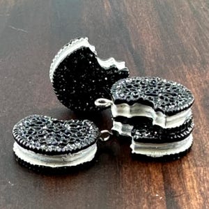 May include: Three black and white cookie charms with a bite taken out of each. The cookies are made of black and white polymer clay and have a shiny finish.