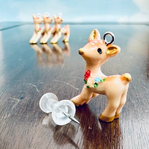 Puede incluir: Una pequeña figurita de ciervo de cerámica de color marrón claro con un diseño floral y detalles dorados. El ciervo está de pie sobre una superficie de madera.