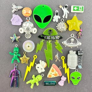 May include: A selection of colourful charms with diverse designs. Includes green alien heads, a UFO, a pizza slice, a lightning bolt, a star, and the word "BELIEVE". The charms are in various colours and sizes.