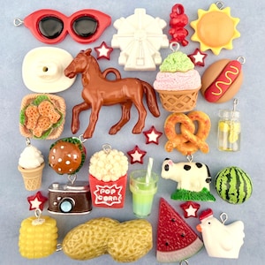 Könnte beinhalten: Eine Sammlung bunter Harzanhänger mit verschiedenen Sommer- und Jahrmarkt-Themen. Enthält ein braunes Pferd, rote Sonnenbrillen, ein Riesenrad, Eiscreme, Hotdog, Popcorn und eine Wassermelonen-Scheibe.