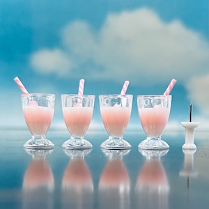 May include: Four clear glass cups filled with pink liquid and topped with pink and white striped straws. The cups are sitting on a table.