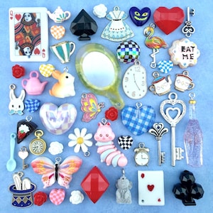 Puede incluir: Una colección de dijes y cabujones variados con temas de Alicia en el país de las maravillas, que incluye una carta de la Reina de Corazones, un espejo, un reloj de bolsillo, un flamenco, un conejo, una oruga, llaves, teteras, corazones y mariposas.