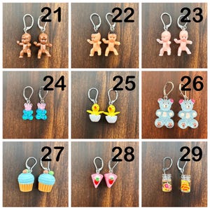 May include: Nine pairs of earrings with various charms, including babies, gummy bears, chicks, teddy bears, cupcakes, and jars of fruit. Each pair is numbered 21 through 29.