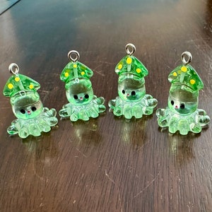 May include: Four green glass octopus charms with yellow mushroom hats. Each octopus has a silver loop for hanging.