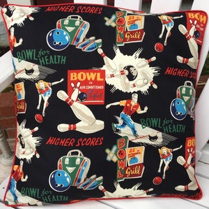 May include: A black and white pillow with a red border features a bowling theme. The pillow has a repeating pattern of bowling pins, bowling balls, bowling bags, and text that says "Bowl for Health" and "Higher Scores".