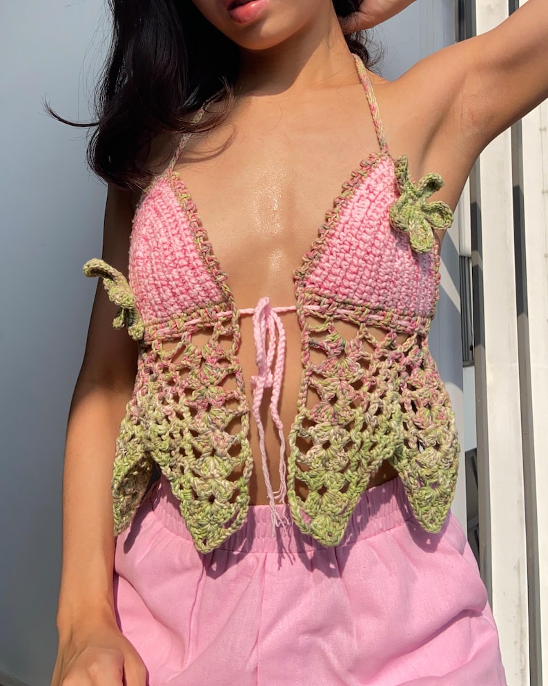 May include: A handmade crochet halter top in pink and green. The top features a tie closure and decorative leaf accents. The openwork design and color palette create a bohemian aesthetic.