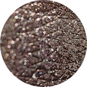 Può includere: Primo piano di un ombretto marrone con un finish shimmer. L'ombretto ha una superficie testurizzata con piccole particelle iridescenti.