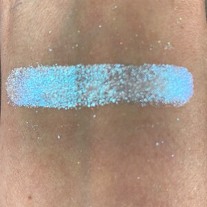 May include: A close-up of a light blue iridescent glitter eyeshadow. The glitter is very fine and has a subtle shimmer.