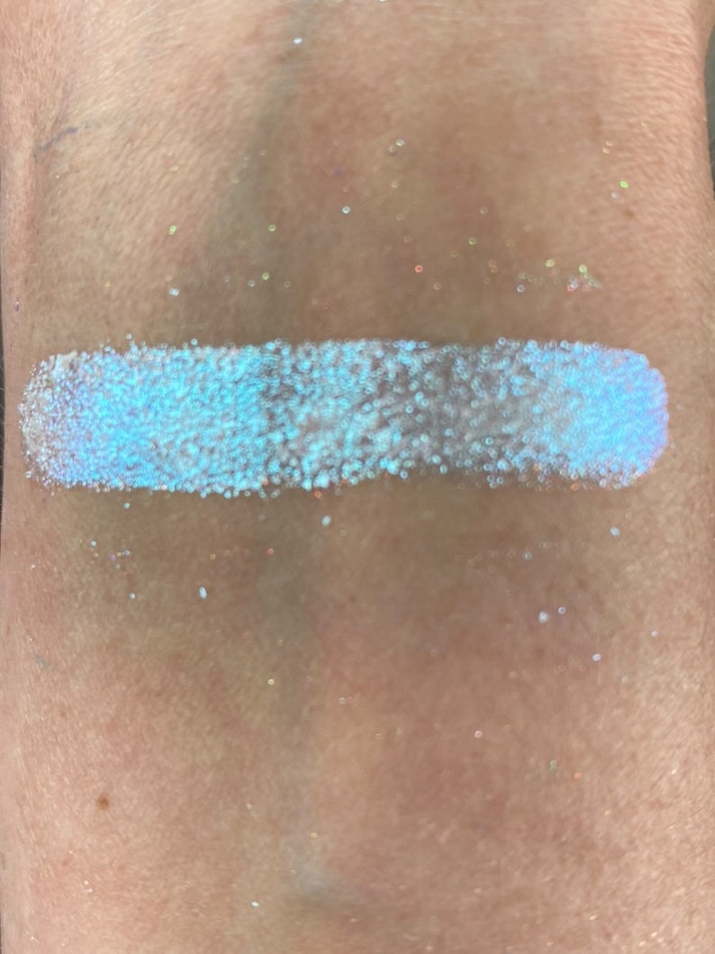 May include: A close-up of a light blue iridescent glitter eyeshadow. The glitter is very fine and has a subtle shimmer.