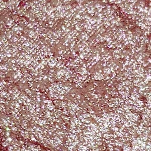 Può includere: Primo piano di un ombretto rosa e bianco glitterato. L'ombretto ha una finitura scintillante e una superficie testurizzata.