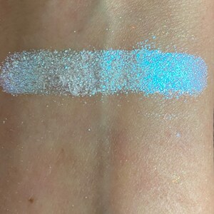 May include: A close-up of a light blue iridescent glitter eyeshadow. The glitter is very fine and has a subtle shimmer.