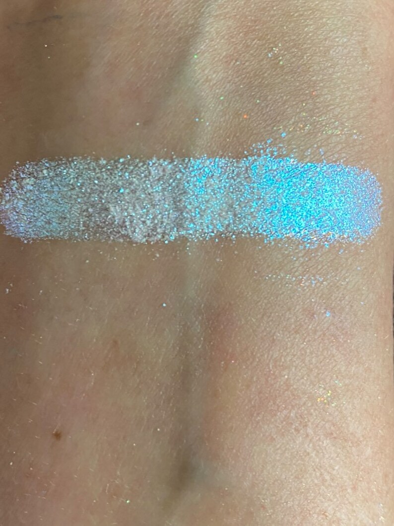 May include: A close-up of a light blue iridescent glitter eyeshadow. The glitter is very fine and has a subtle shimmer.